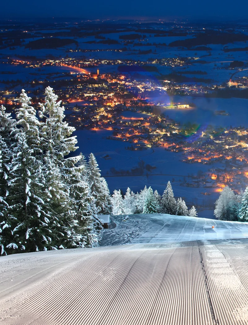 Blick über die beleuchtete Skipiste beim Flutlichtfahren in Pfronten-Steinach mit einem schönen Blick ins Tal.